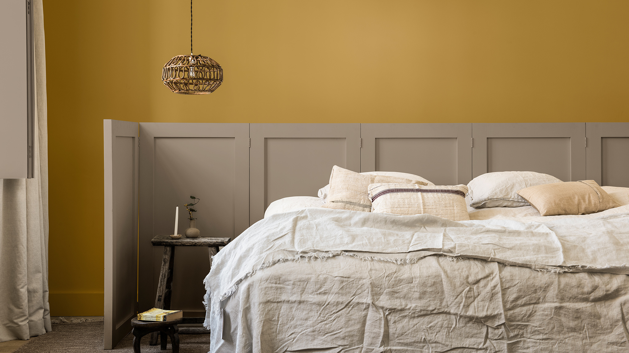 Bedroom wall painted in golden yellow and Brave Ground, with paneled screen behind bed Dulux_CF21_ Colour_of_the_year_Timeless_colors_global_2